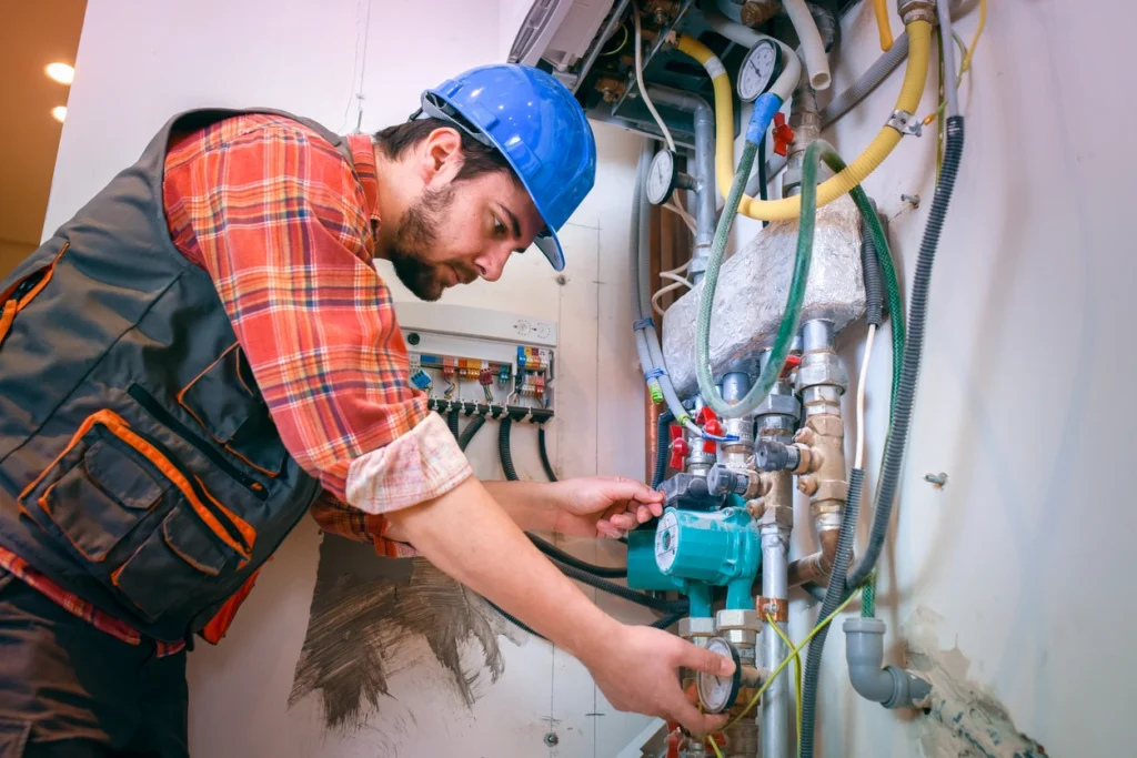 A man wearing a hard hat and safety vest is installing a water heater in a residential setting.